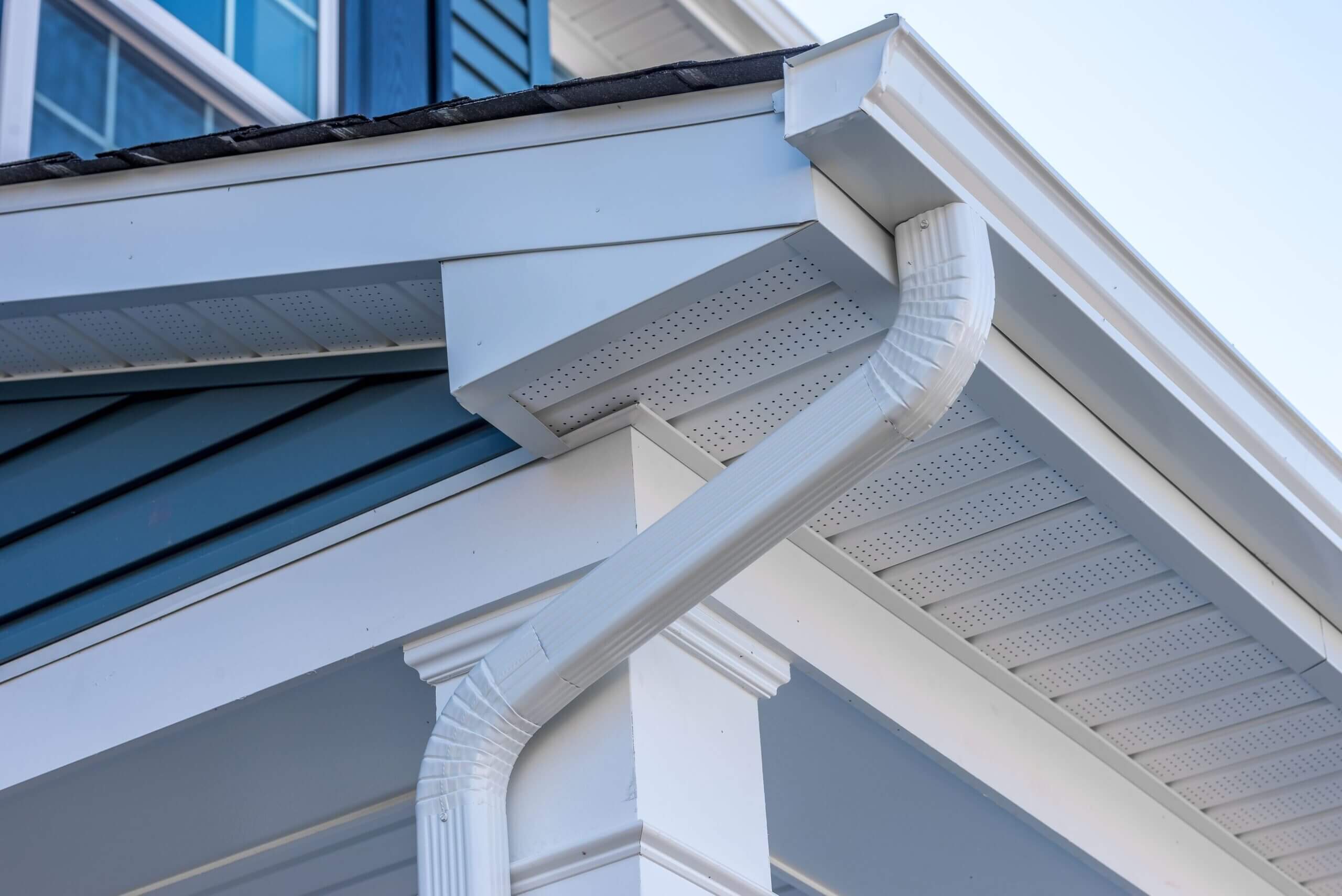Close-up of a white gutter downspout on a house corner.