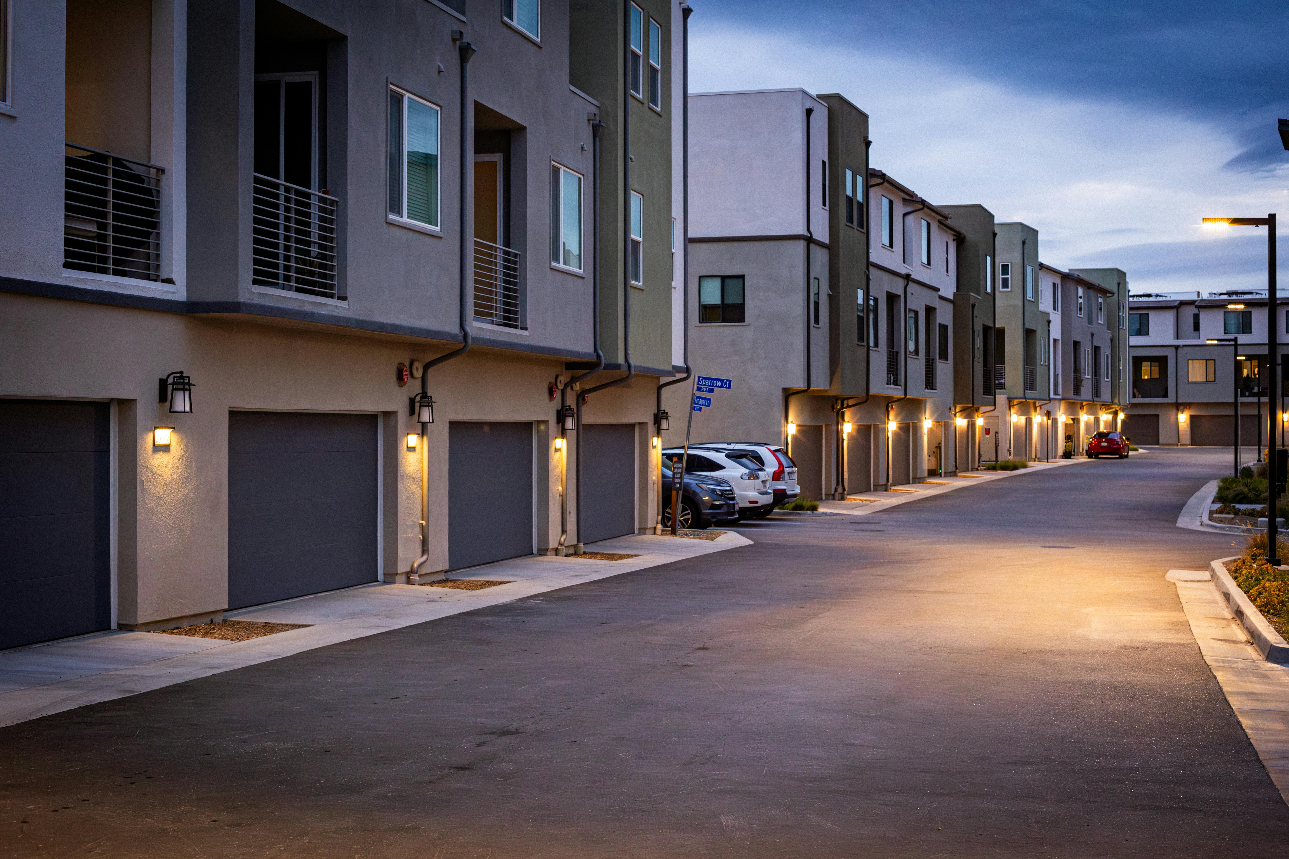 Quiet suburban street with illuminated townhouses at dusk, showcasing modern architectural style.