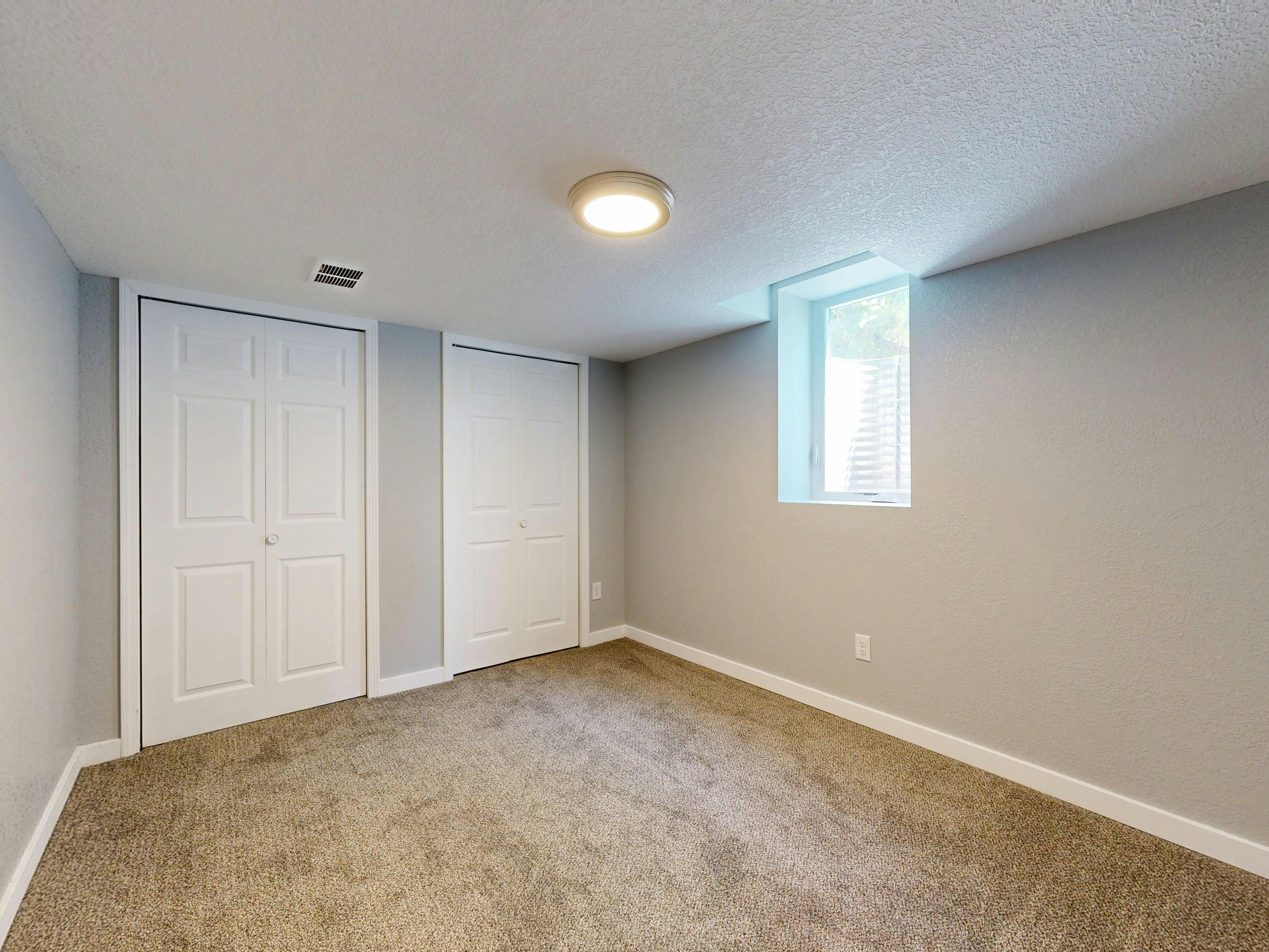 Minimalistic empty room with carpet, two white doors, and natural light from a window.
