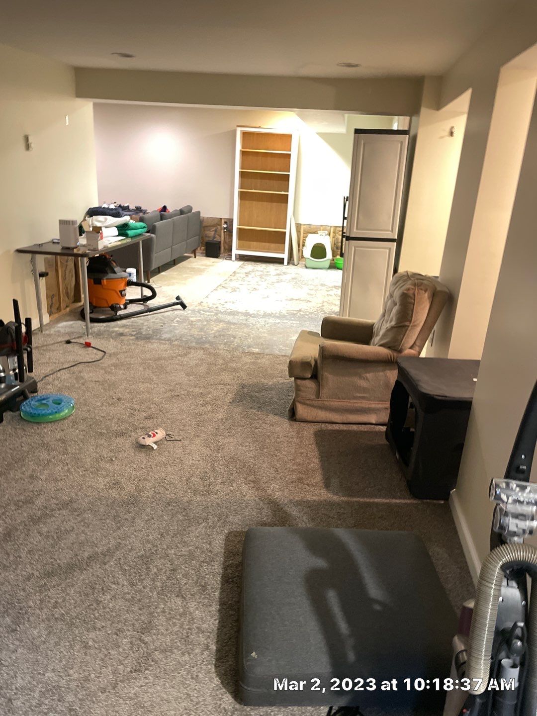 Basement carpeted room with armchair and vacuum